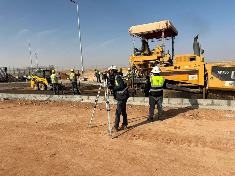 فرّادة أسفلت وطاقم عمل أثناء سفلتة طريق داخل موقع المحطة